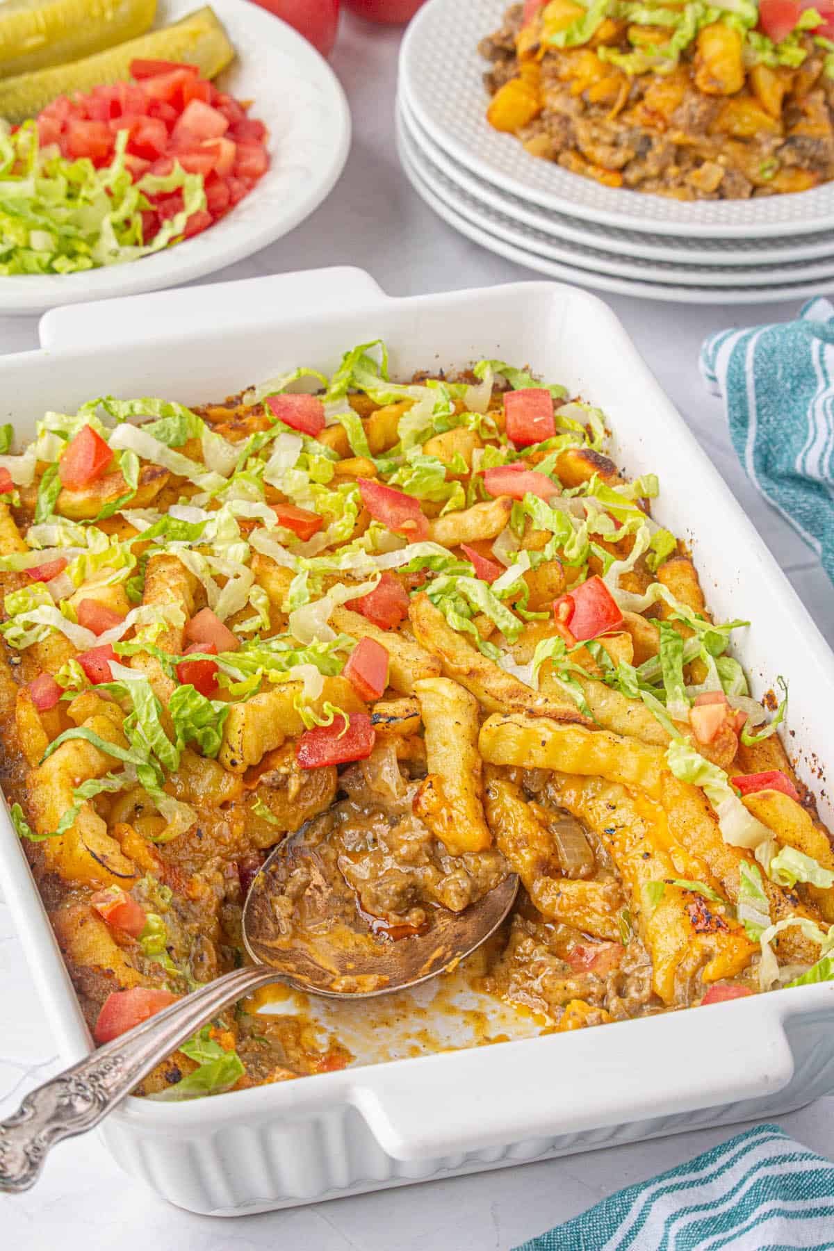 Baking dish filled with a cheeseburger french fry casserole, with a serving spoon.