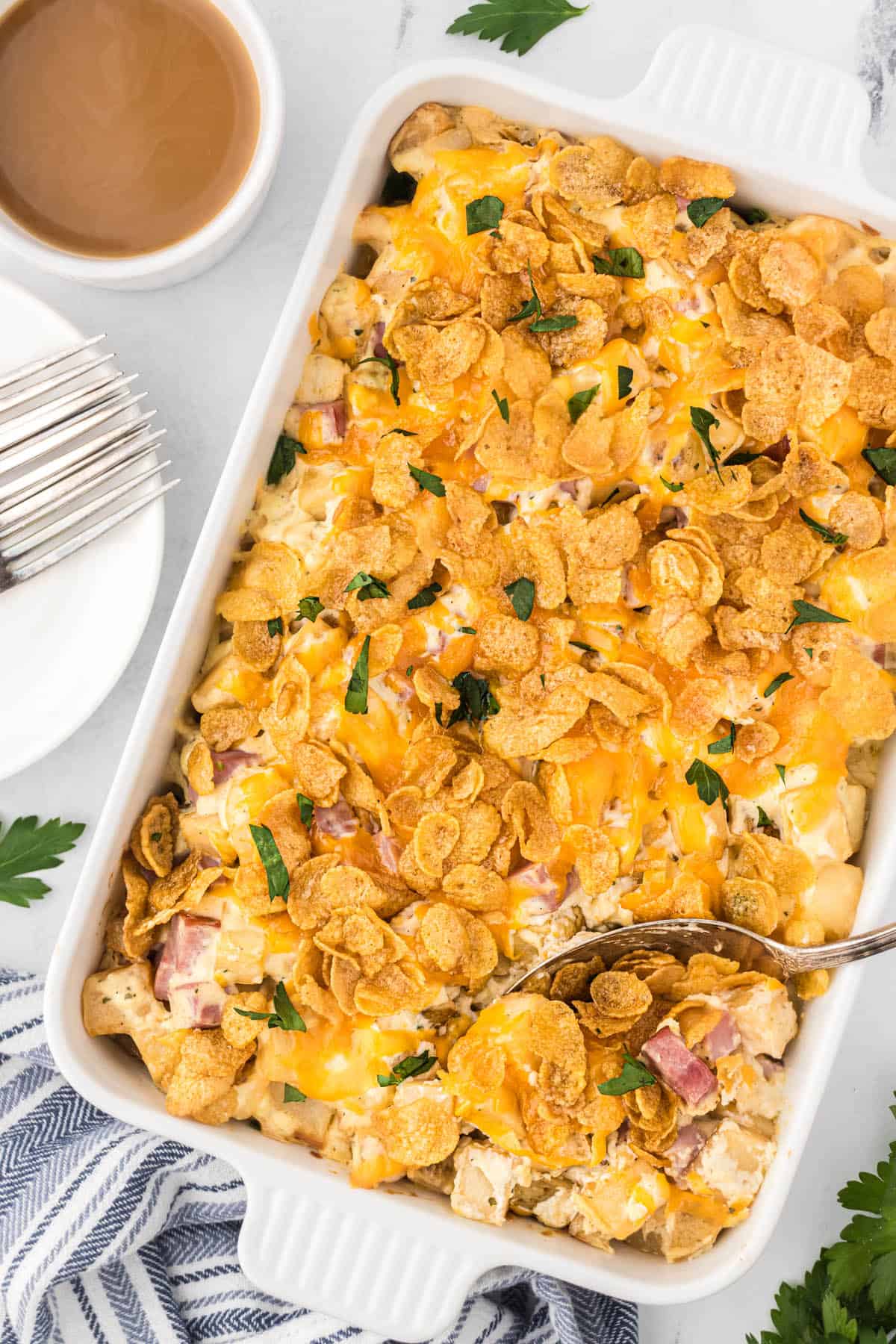 Hashbrown casserole in baking dish, topped with cornflakes. With a serving spoon.