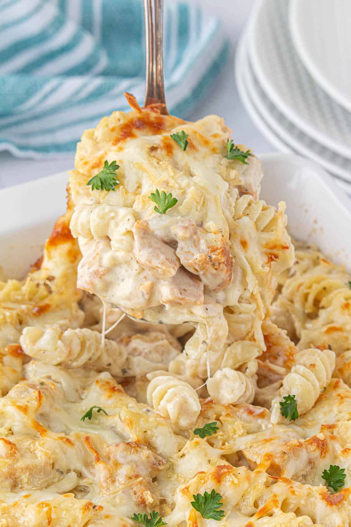 Saucy Garlic Parmesan Chicken Pasta Bake in a casserole dish with a serving spoon scooping up a serving.