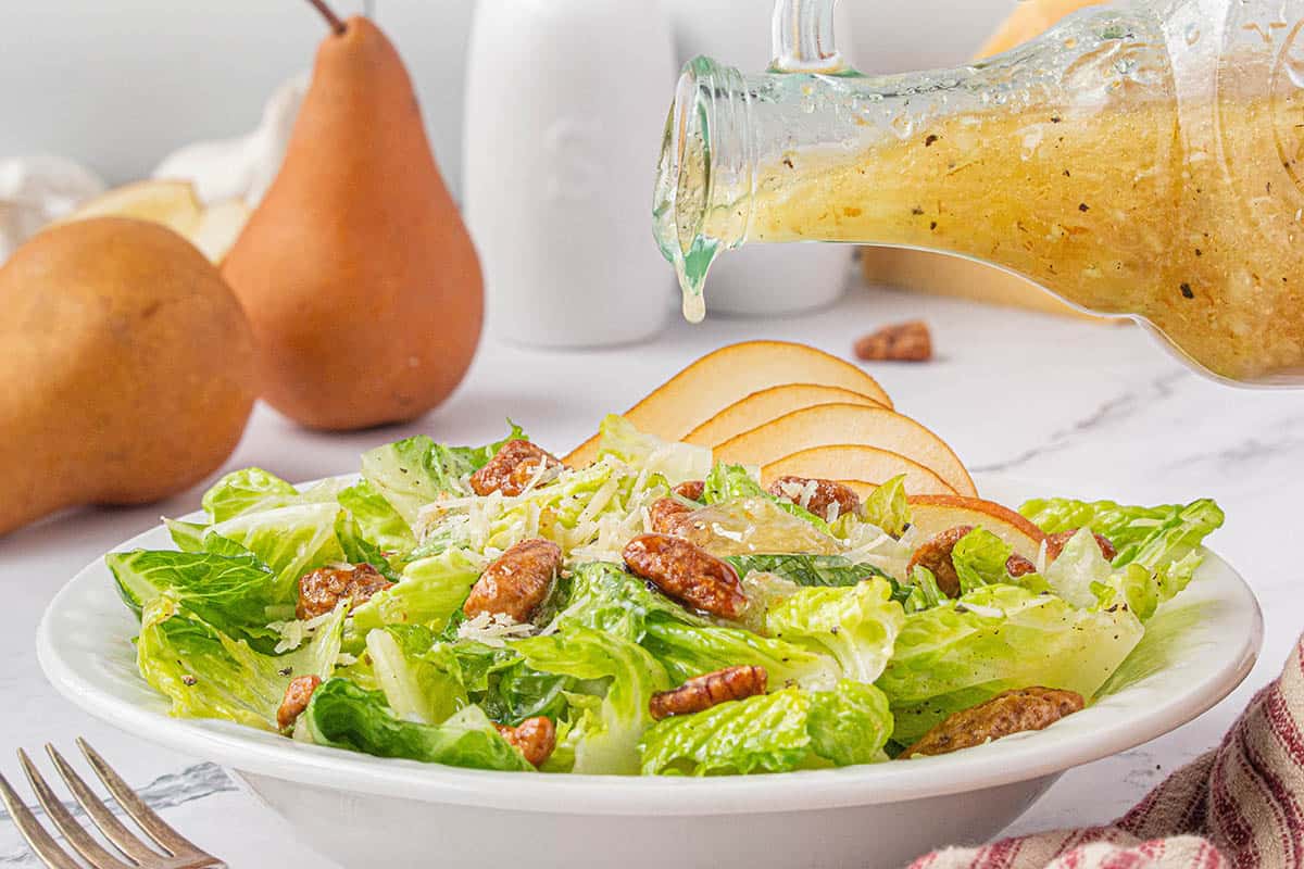 A bowl filled with green salad being topped with a pear vinaigrette.