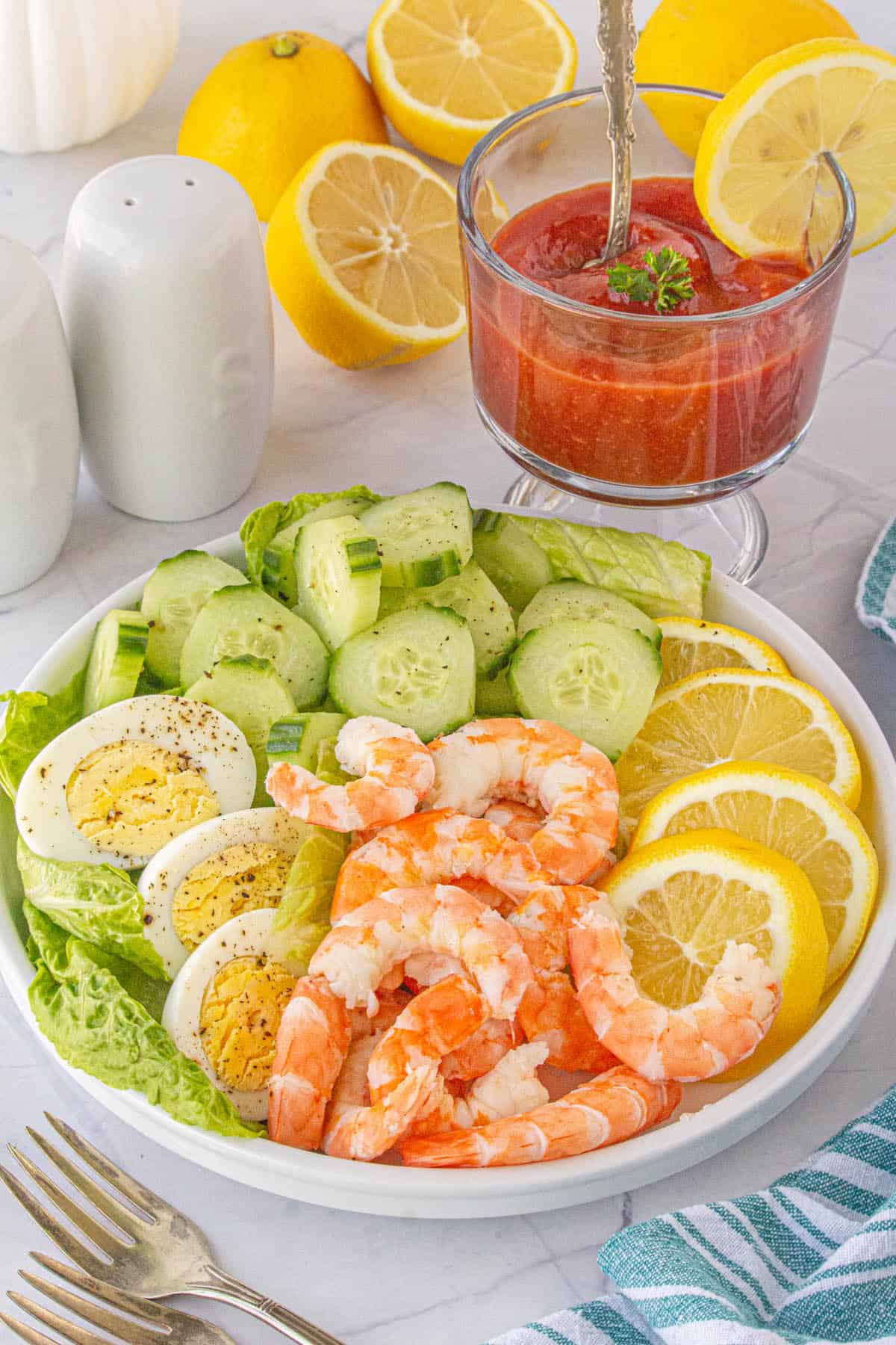 Shrimp, boiled eggs and fresh slices of lemon on a platter with shrimp sauce on the side.