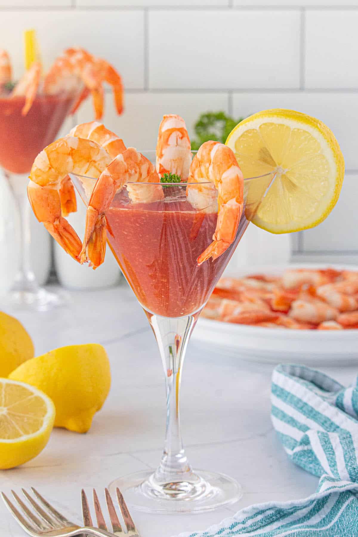 A pretty glass filled with shrimp cocktail sauce. With pretty plump shrimp hanging over the edges of the glass. Lemon is used for garnish on the glass.