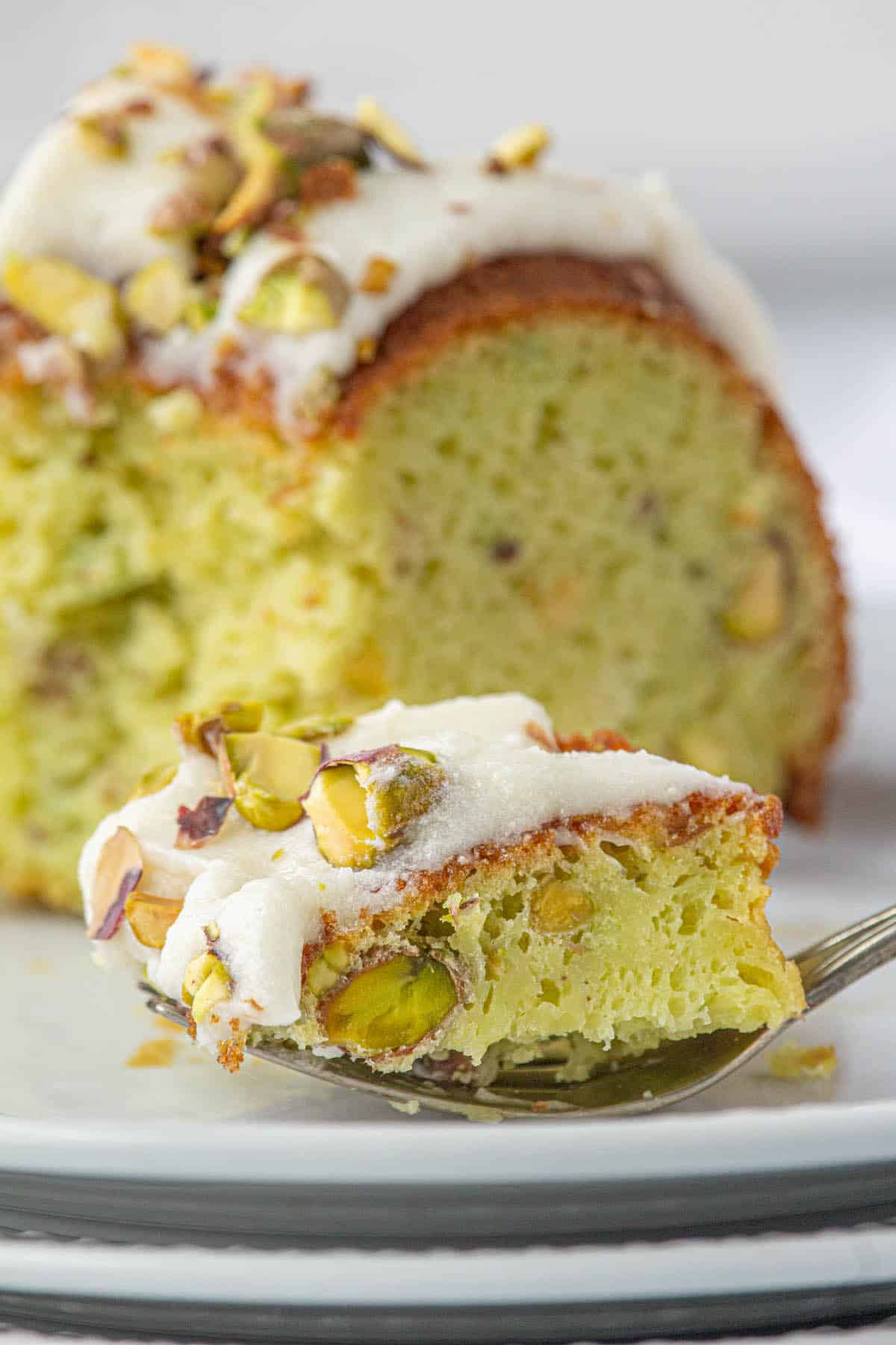 A slice of Pistachio Bundt Cake on a plate with a fork that is filled with a bite of cake.