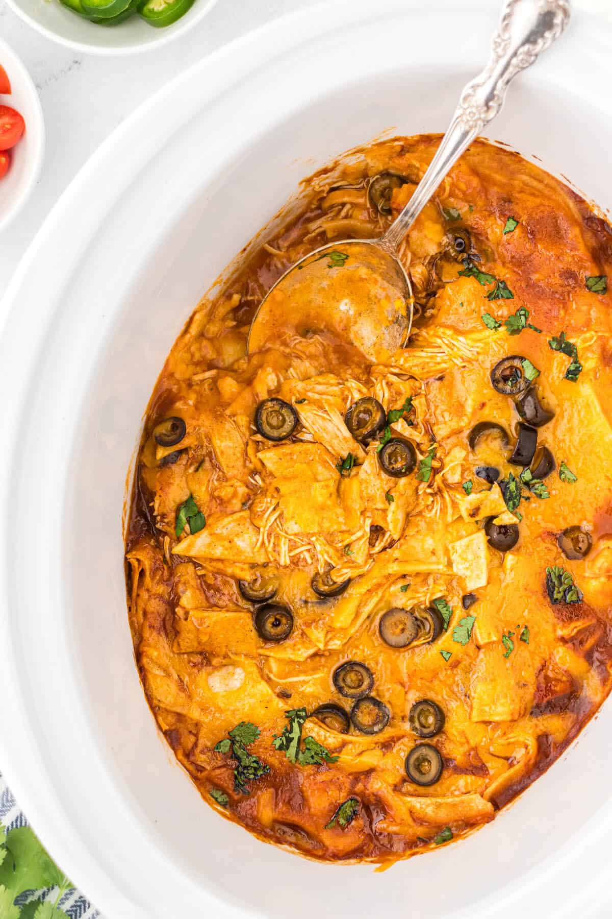 Crockpot chicken enchilada casserole in a slow cooker with a serving spoon.