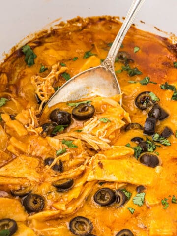 Crockpot filled with chicken enchilada casserole with a serving spoon.