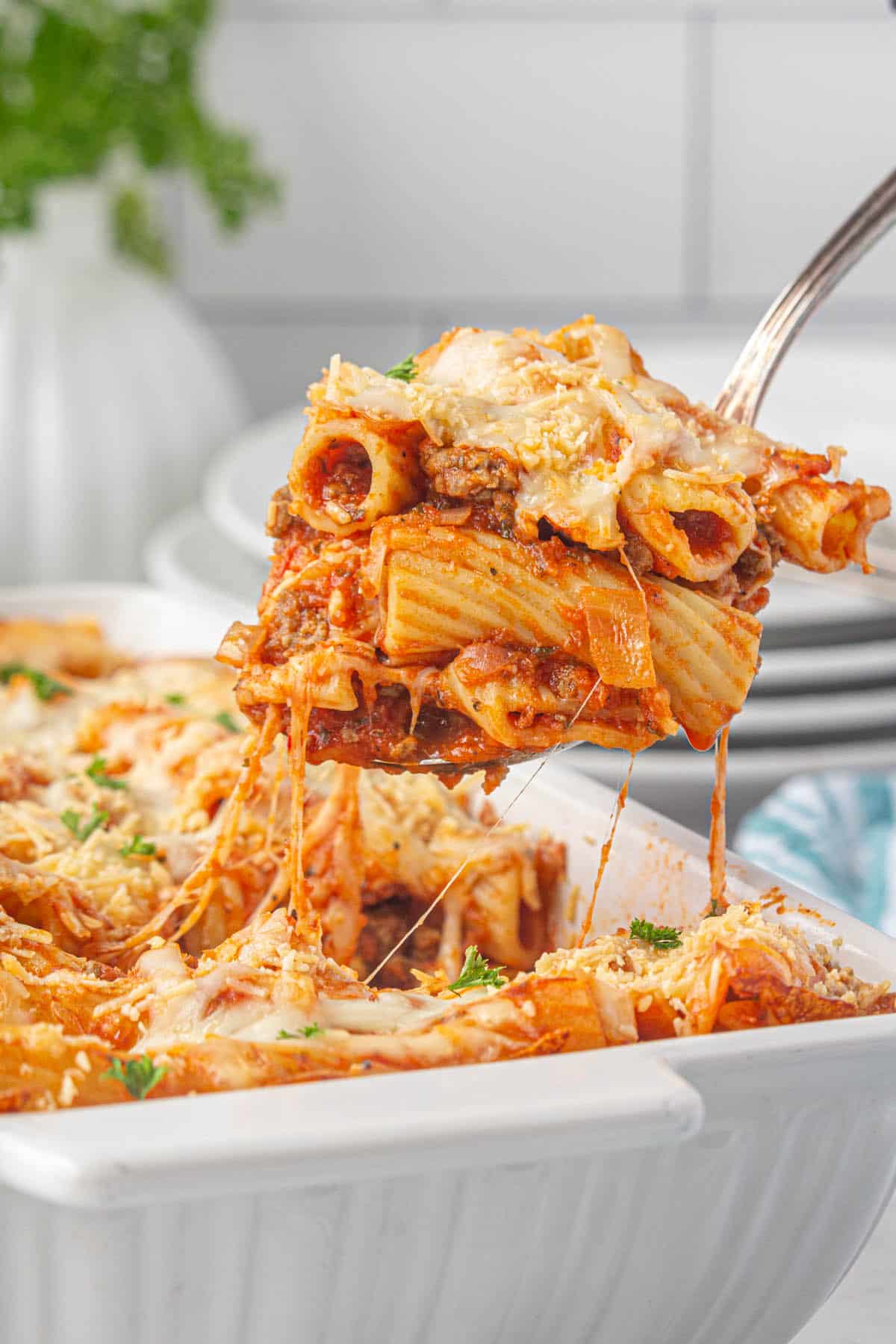 Cheesy pasta casserole in a baking dish with a serving spoon taking a scoop.