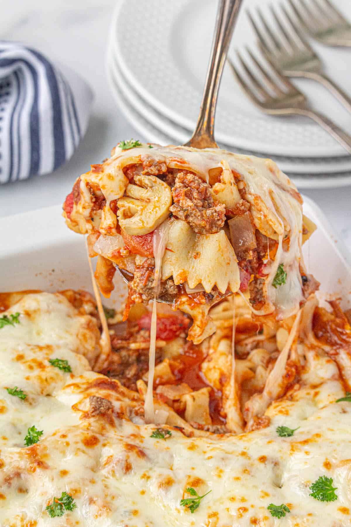 Baked pasta in a casserole dish with a serving spoon taking a big scoop.
