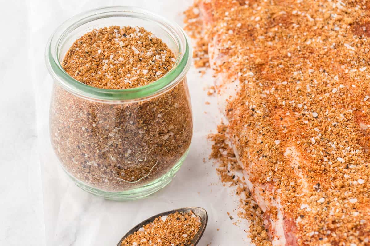 Seasoning for ribs on a slab of ribs, with a jar of spice mix off to the side.
