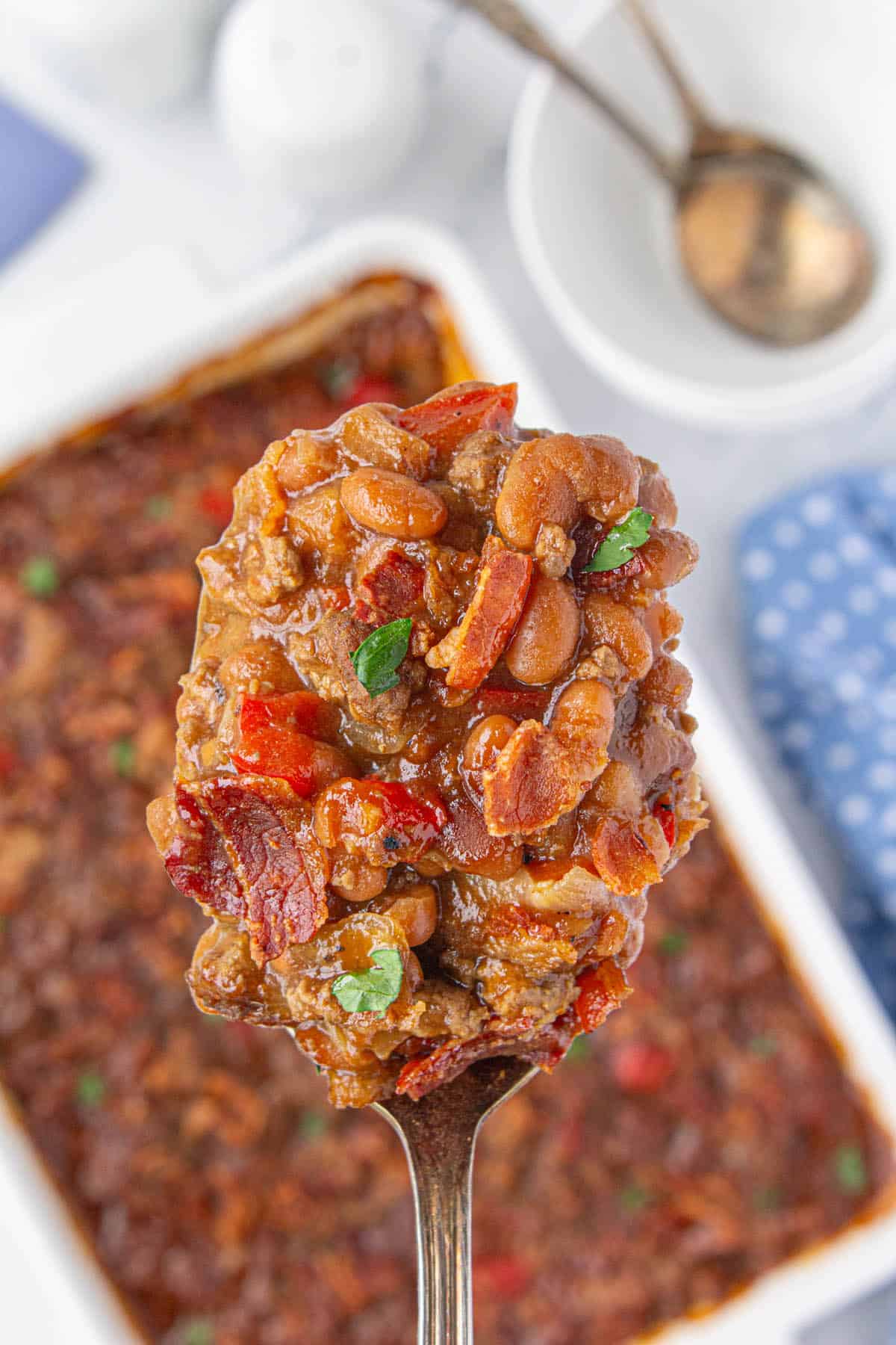 A big casserole dish filled with brown sugar baked beans. There's a close-up of a spoon holding a scoop of the beans.