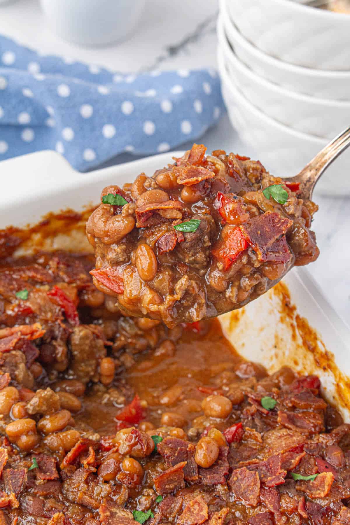 Brown sugar baked beans in a casserole dish. A serving spoon is scooping some out.