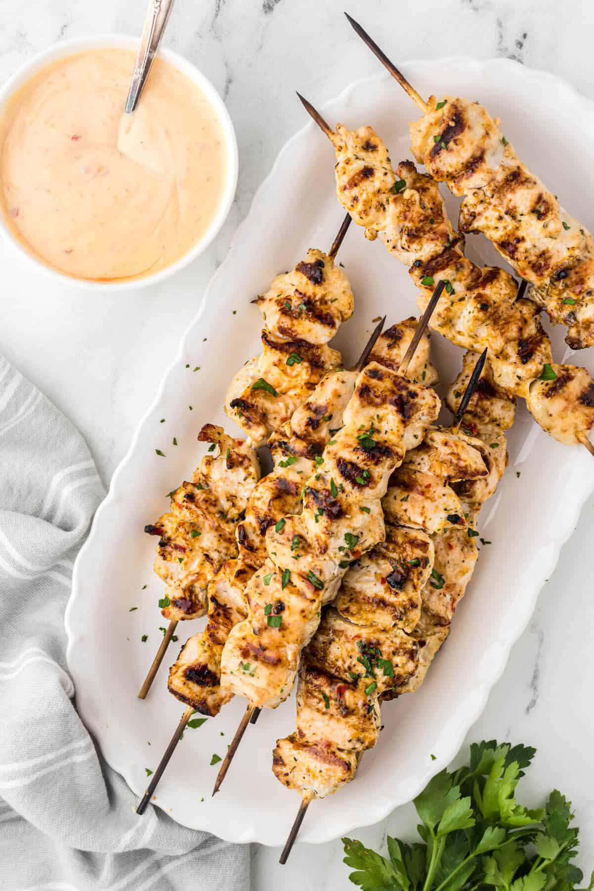A platter of bang bang chicken skewers on a platter beside a bowl of dipping sauce.