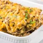 Cheesy ground beef and rice casserole in baking dish with a spoon taking a big scoop.