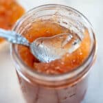 An opened jar of rhubarb pineapple jam with a spoon in it to scoop out the jam.