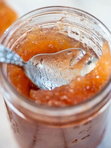 An opened jar of rhubarb pineapple jam with a spoon in it to scoop out the jam.