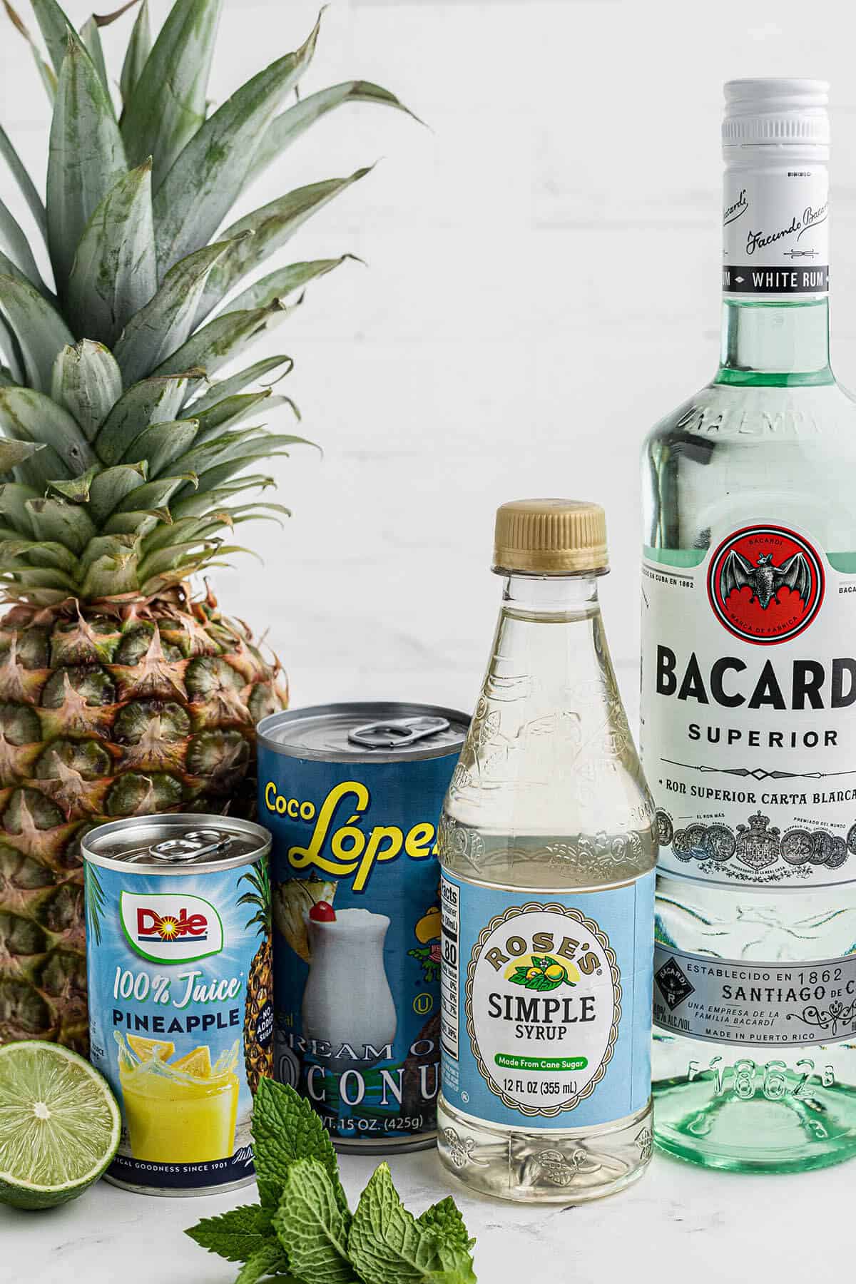 Ingredients to make the cocktail; pineapple juice, cream of coconut, simple syrup, lime and light rum.