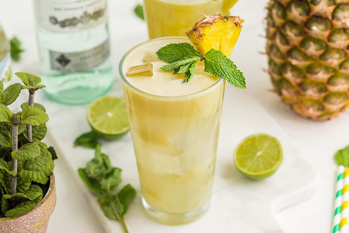 Pineapple crush cocktail with a fresh pineapple on the side, mint, lime and light rum.