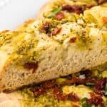 Sliced focaccia bread topped with pesto, sun-dried tomatoes and fresh basil. With print overlay for Pinterest.