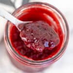 Cherry jam in a jar with a spoon scooping out jam.