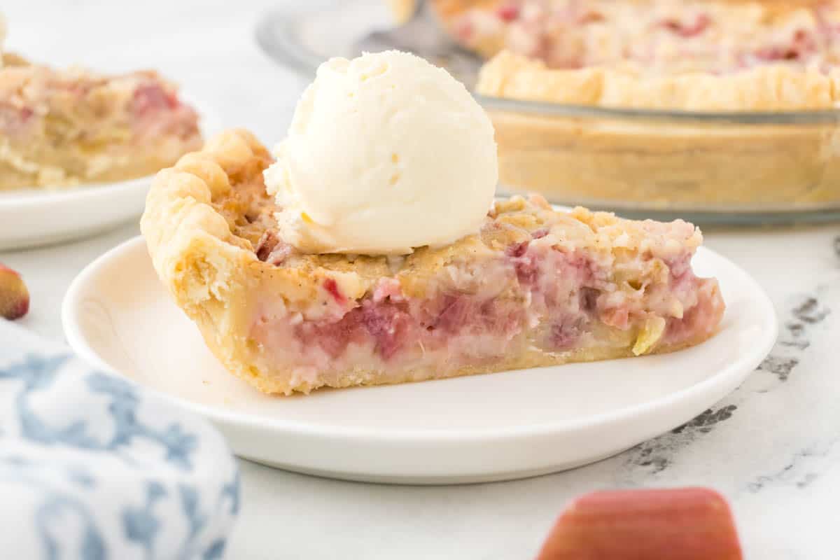 A slice of cream rhubarb pie on a plate topped with ice cream.