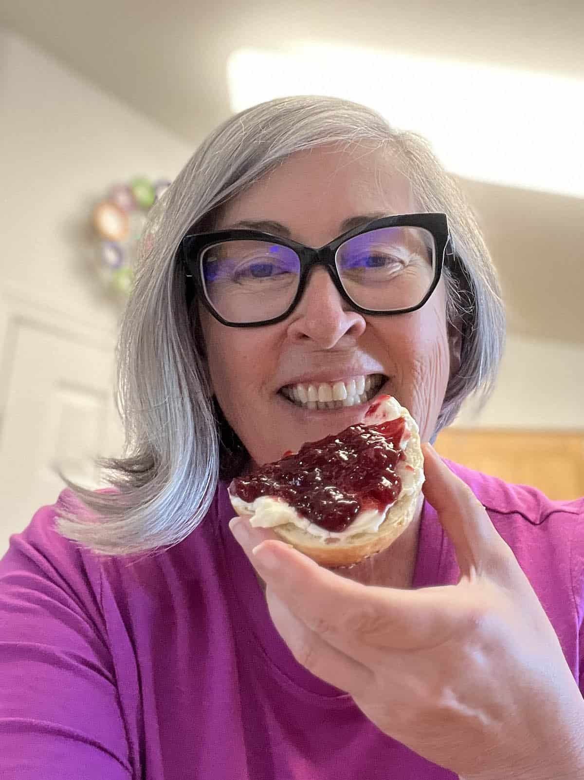 Deb eating a bagel topped with cream cheese and cherry jam.
