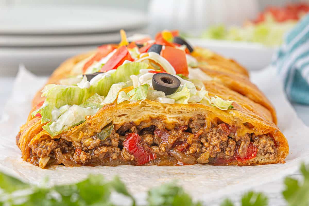 Fajita Taco Braid Recipe with Crescent rolls. The braid is baked until golden brown, and topped with lettuce, tomatoes and olives.