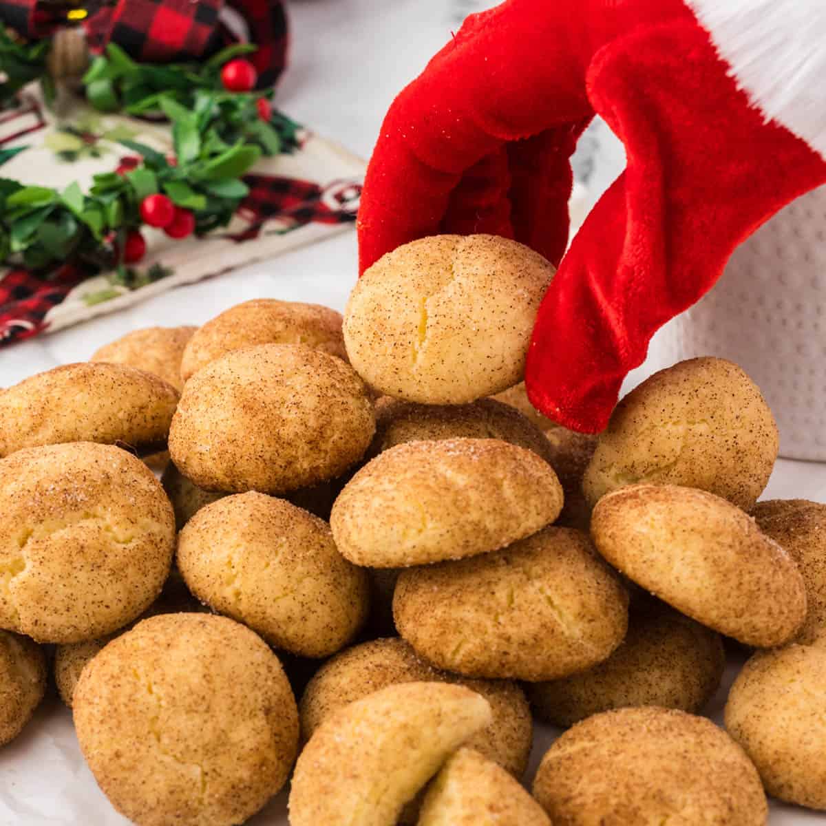 A large pile of cookies on a platter. A gloved hand that looks like Santa is reaching down to grab a cookie.