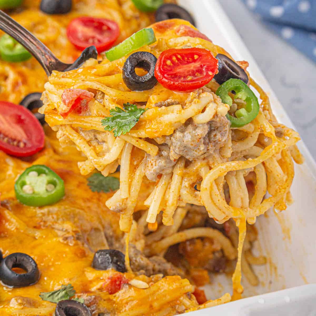 Cheesy taco spaghetti casserole with a spoon scooping out a serving.