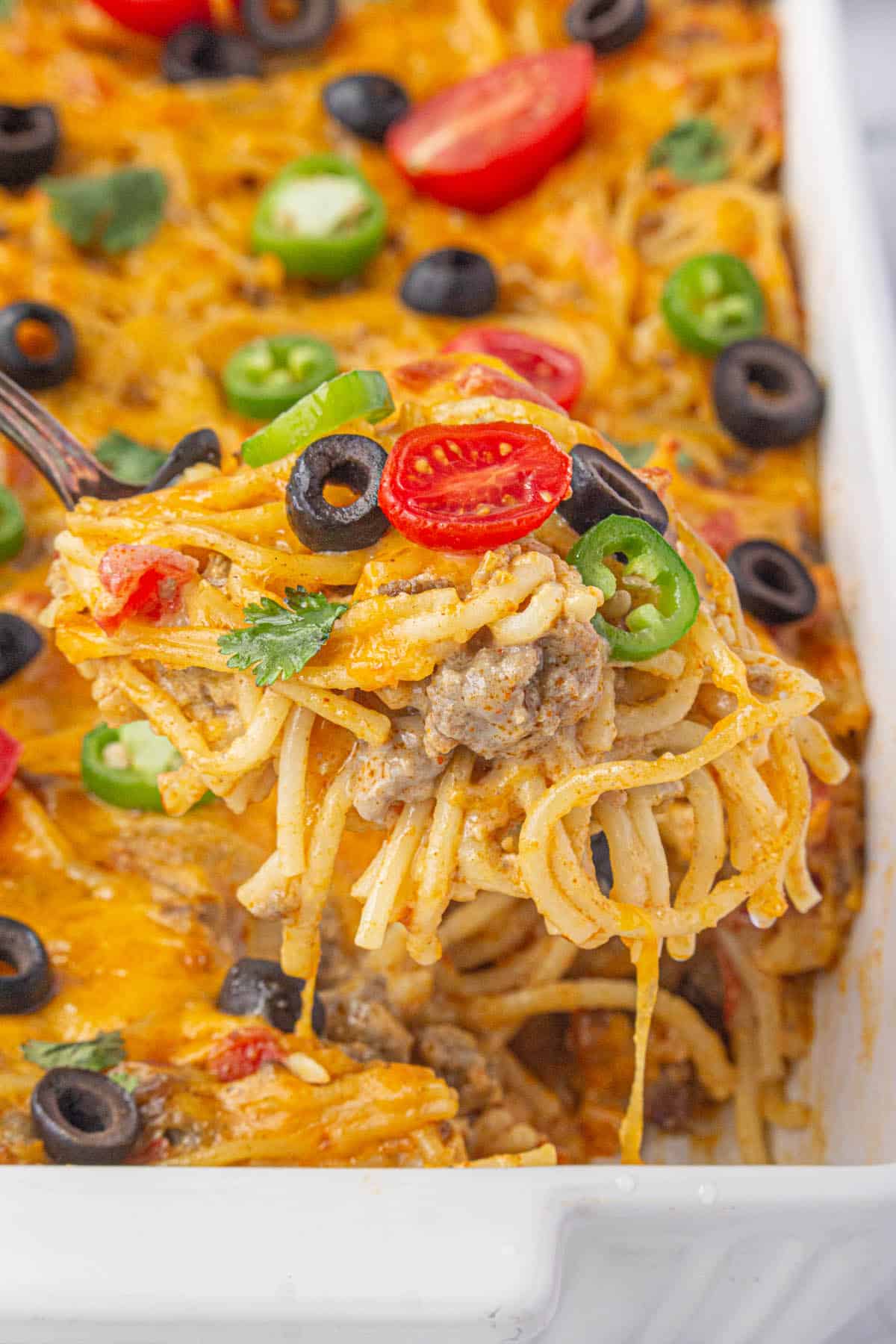 Spaghetti taco casserole in a baking dish, with a serving spoon scooping out a serving.