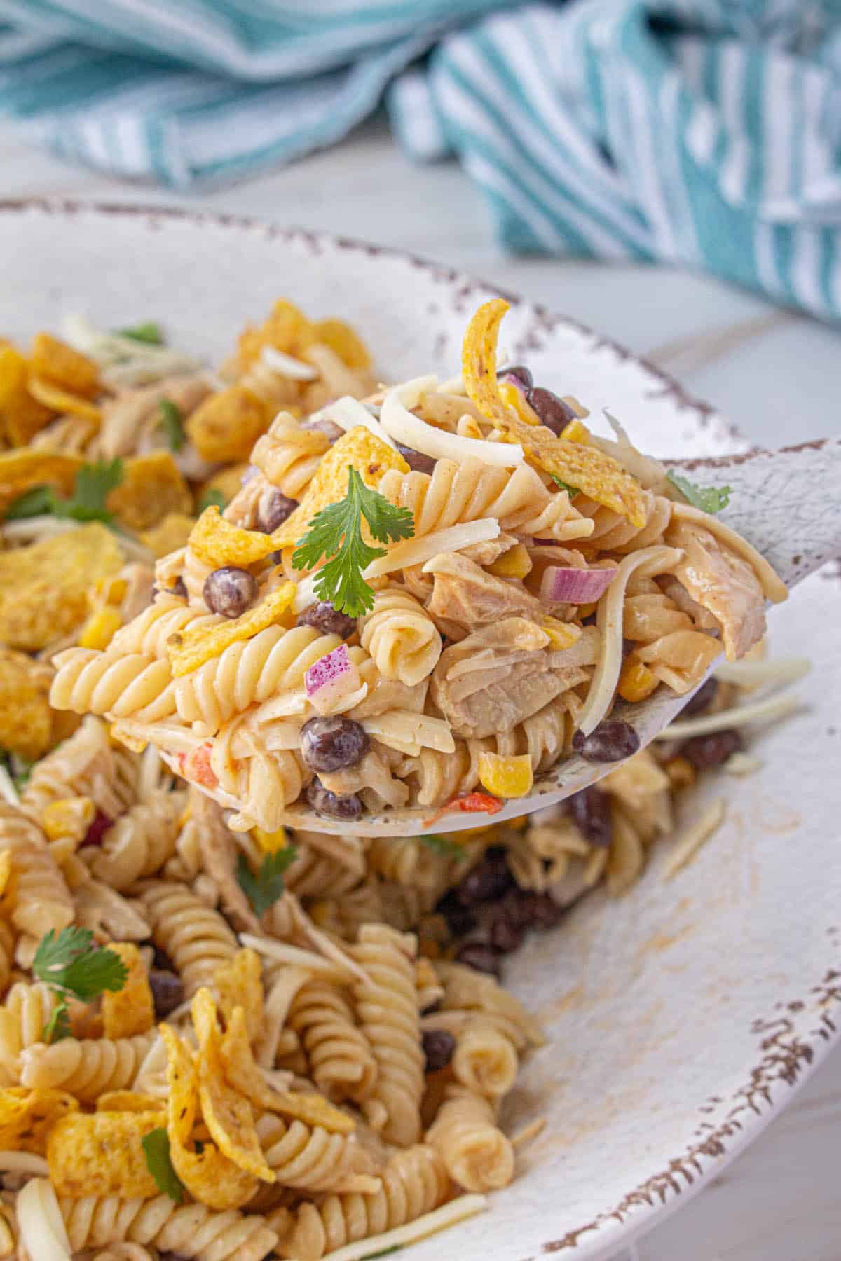 A bowl filled with bbq chicken pasta salad, with a spoon taking a big scoop out.