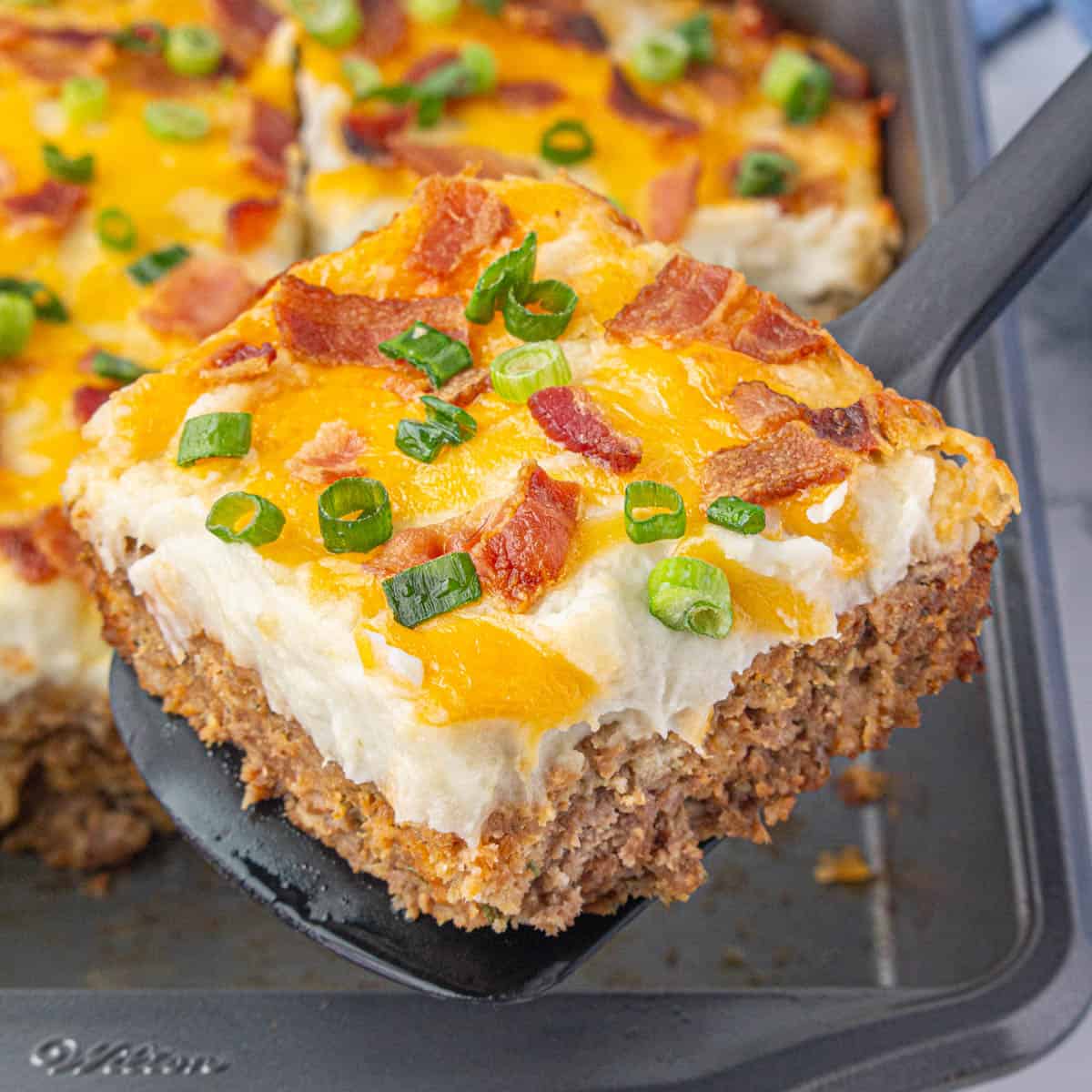 Meatloaf potato casserole in a baking dish. With a spatula dishing up a serving.