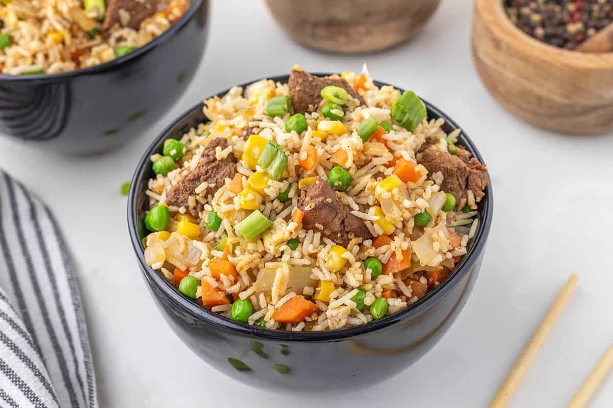 A black bowl filled withfried rice and steak.