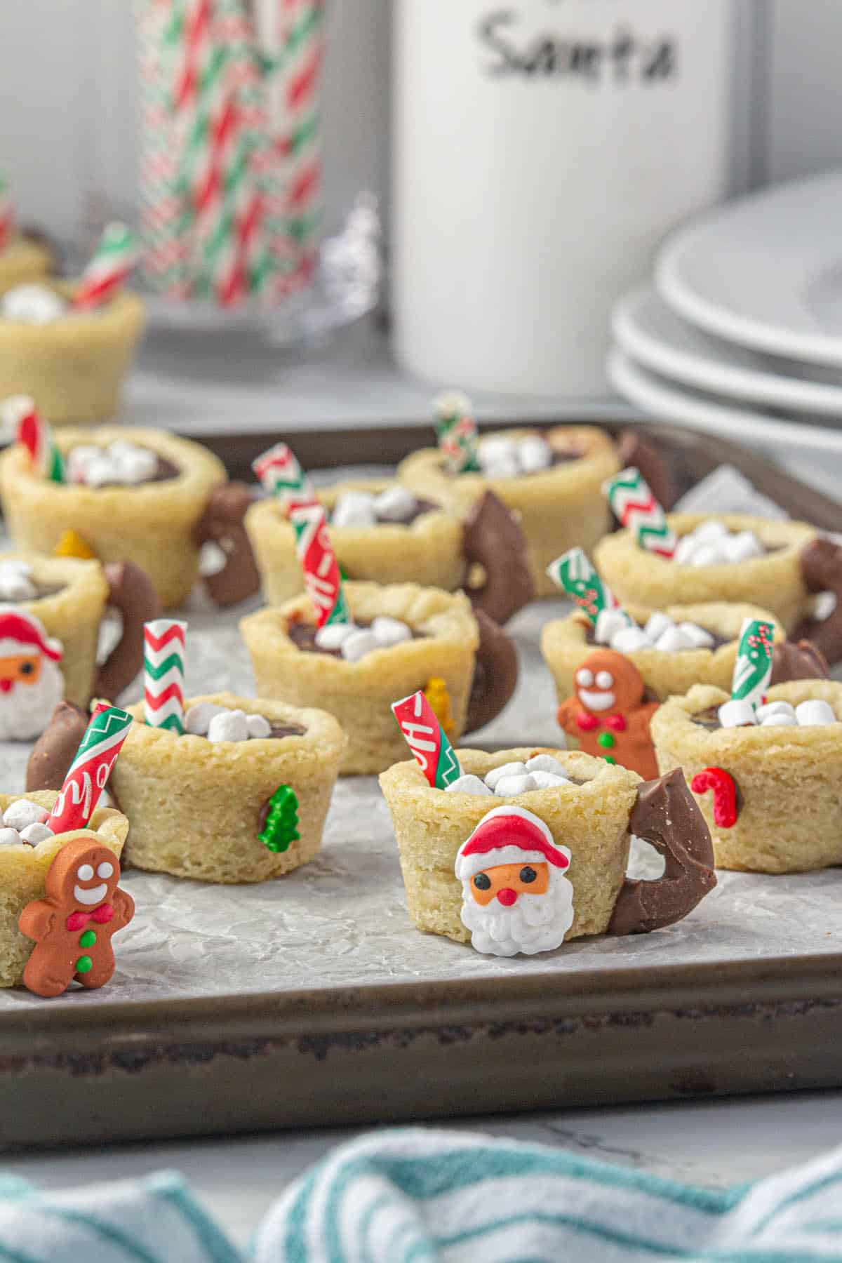 The cutest hot chocolate cookies cups decorated with Christmas candies scattered on a baking sheet.