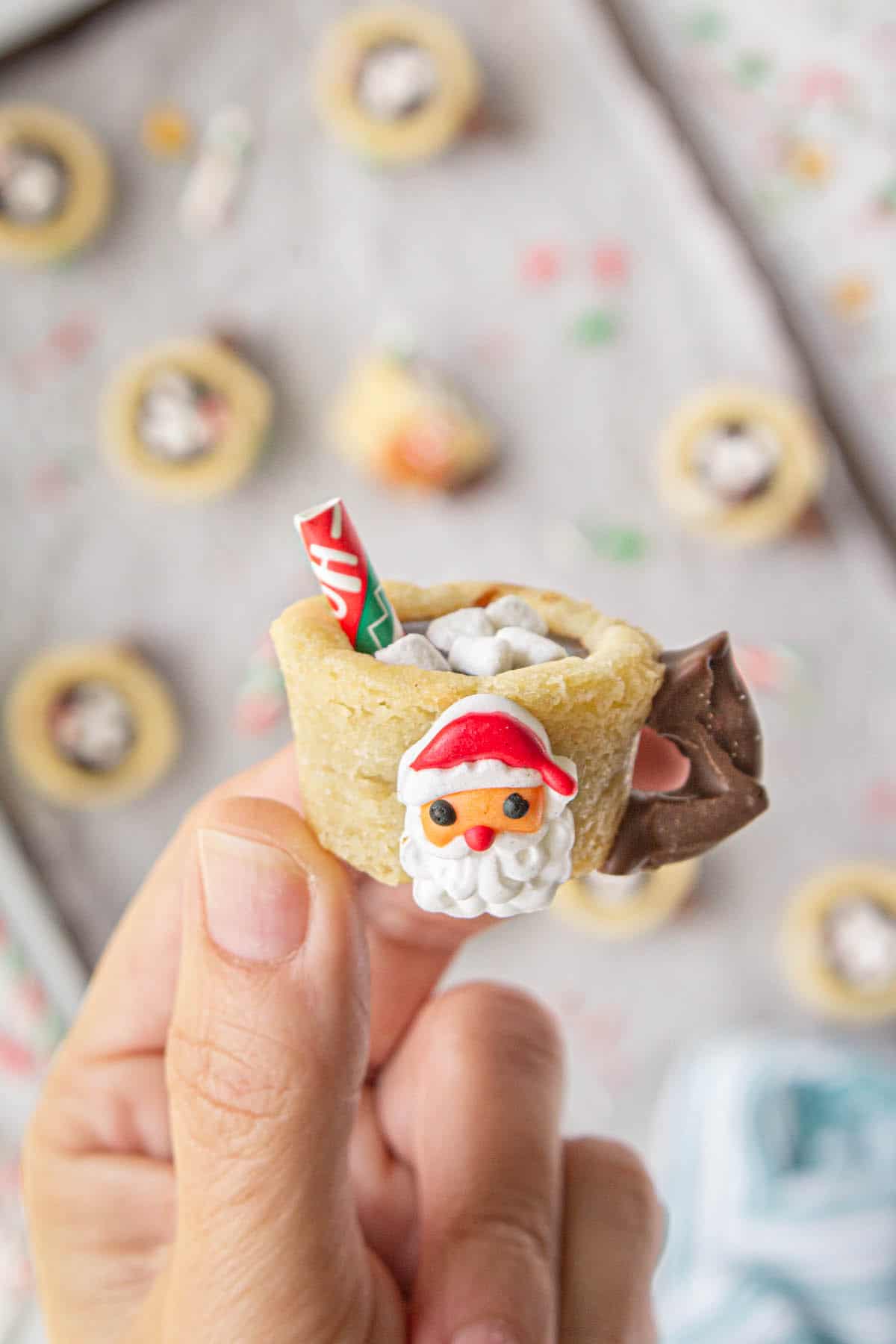 A hand holding a hot chocolate cookie mug decorated with a Santa candy.