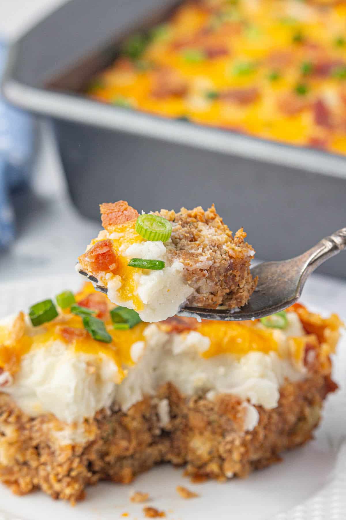 A serving of meatloaf potato casserole on a plate with a fork taking a bite.