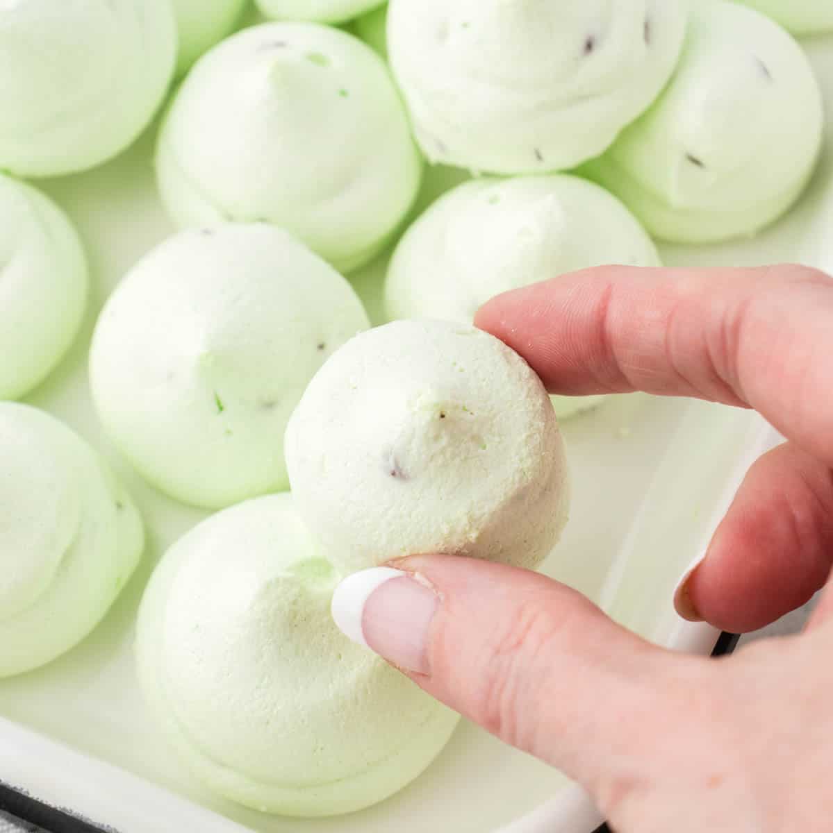 A platter of Chocolate Chocolate Meringue Cookies with a hand holding a cookie.