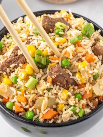 Steak fried rice in a bowl, with a pair of chopsticks grabbing a bite.