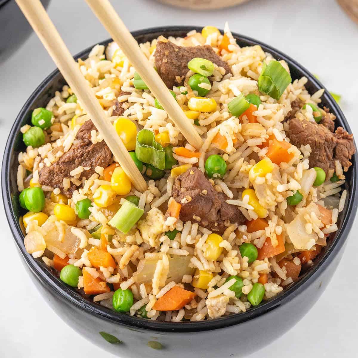 Steak fried rice in a bowl, with a pair of chopsticks grabbing a bite.