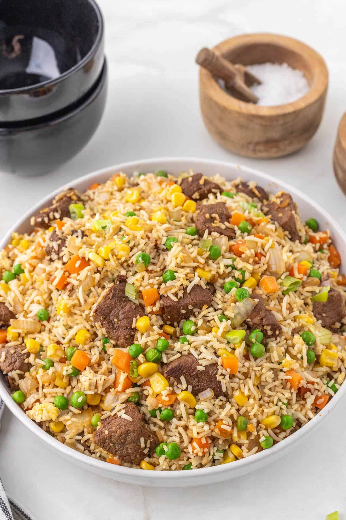 A big bowl filled with steak fried rice with bowls in the background for serving.