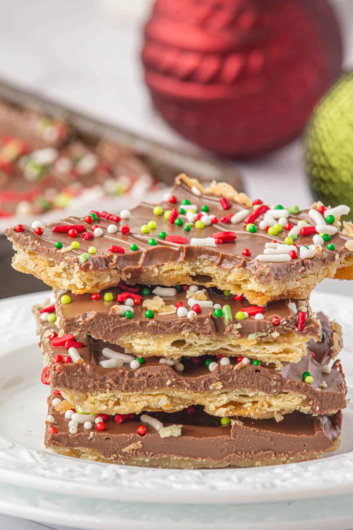 A stack of Toffee made with saltine crackers on a plate. One piece of candy has a bite taken out of it.