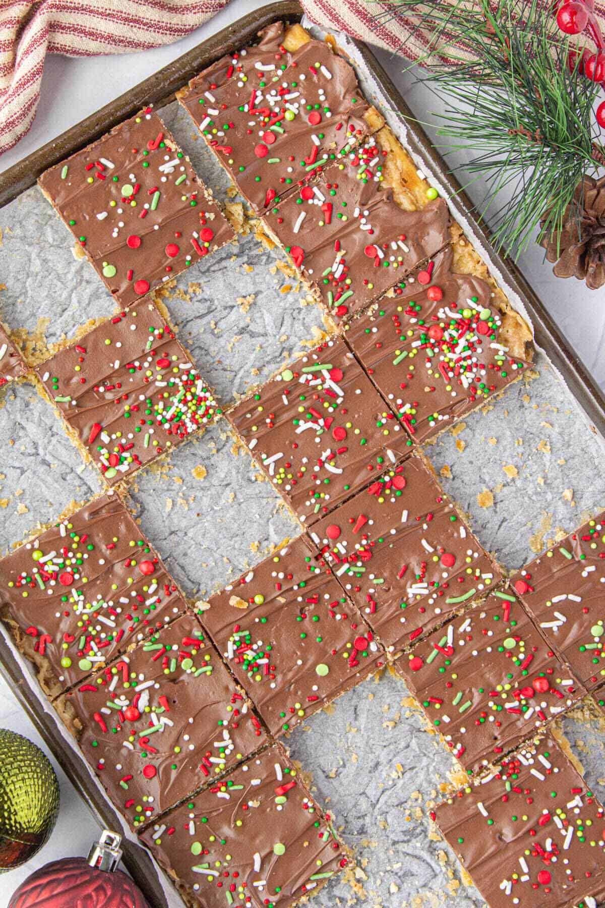 Toffee saltine crackers topped with holiday sprinkles on a sheet pan cut up into squares.