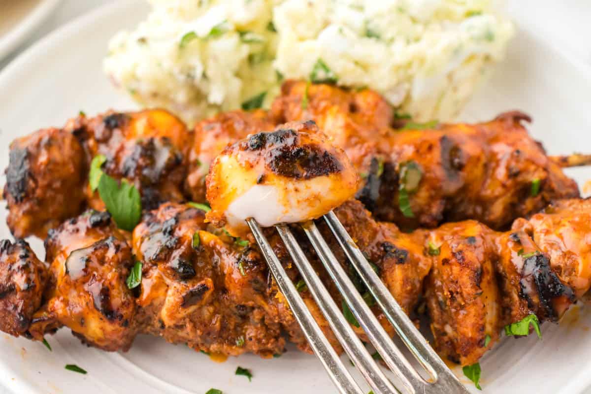 BBQ Chicken skewers on a platter with a fork holding a piece of chicken.