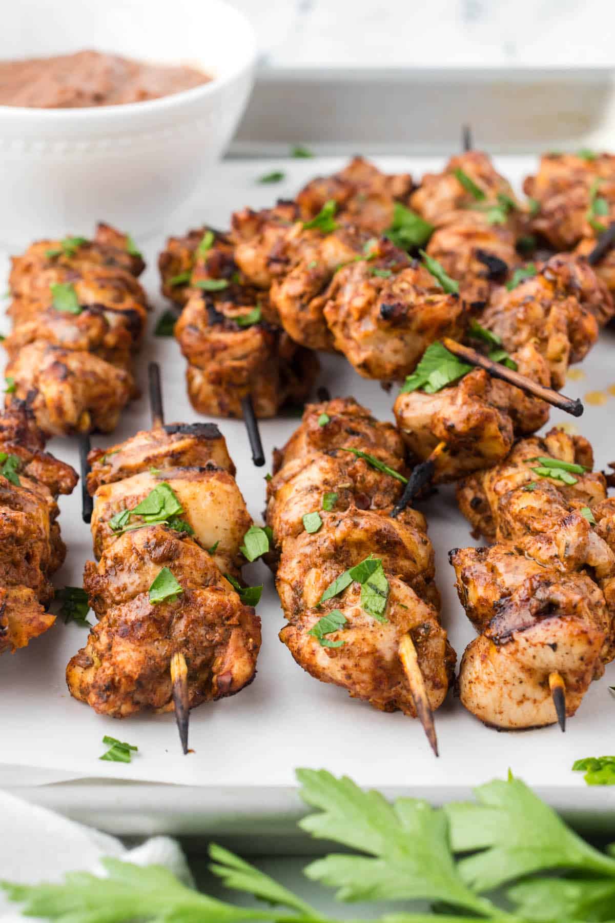 BBQ Chicken Skewers appetizers on a platter with extra sauce for dipping.