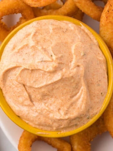 Blooming onion sauce in a bowl surrounded by crispy onion rings.