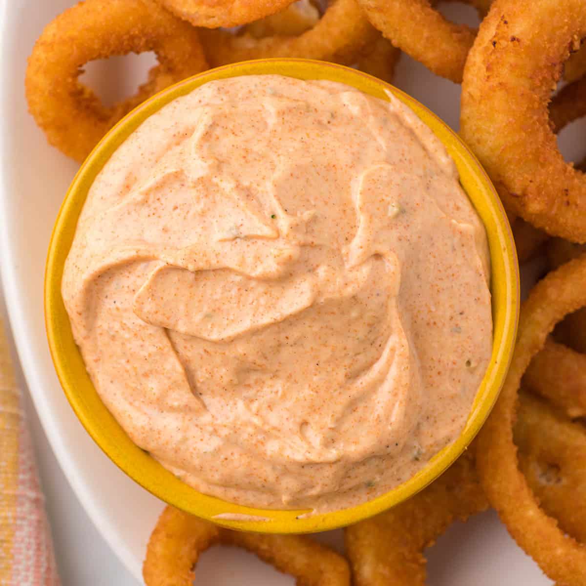 Blooming onion sauce in a bowl surrounded by crispy onion rings.