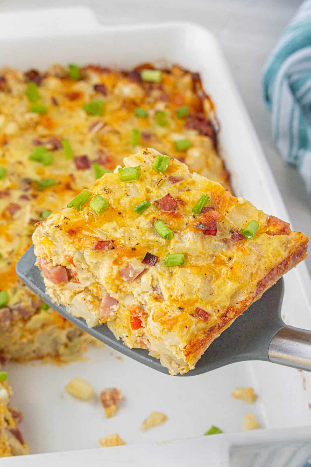 Ham hashbrown breakfast casserole in a baking dish, with a spatula dishing up a slice.