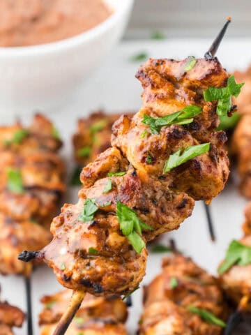 Skewers of bbq chicken on a platter with dipping sauce.