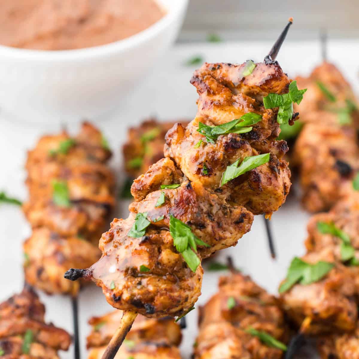 Skewers of bbq chicken on a platter with dipping sauce.