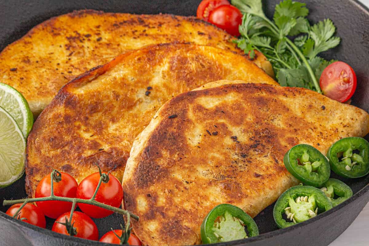 Three cheesy quesadillas with filled with ground beef in a cast iron skillet.