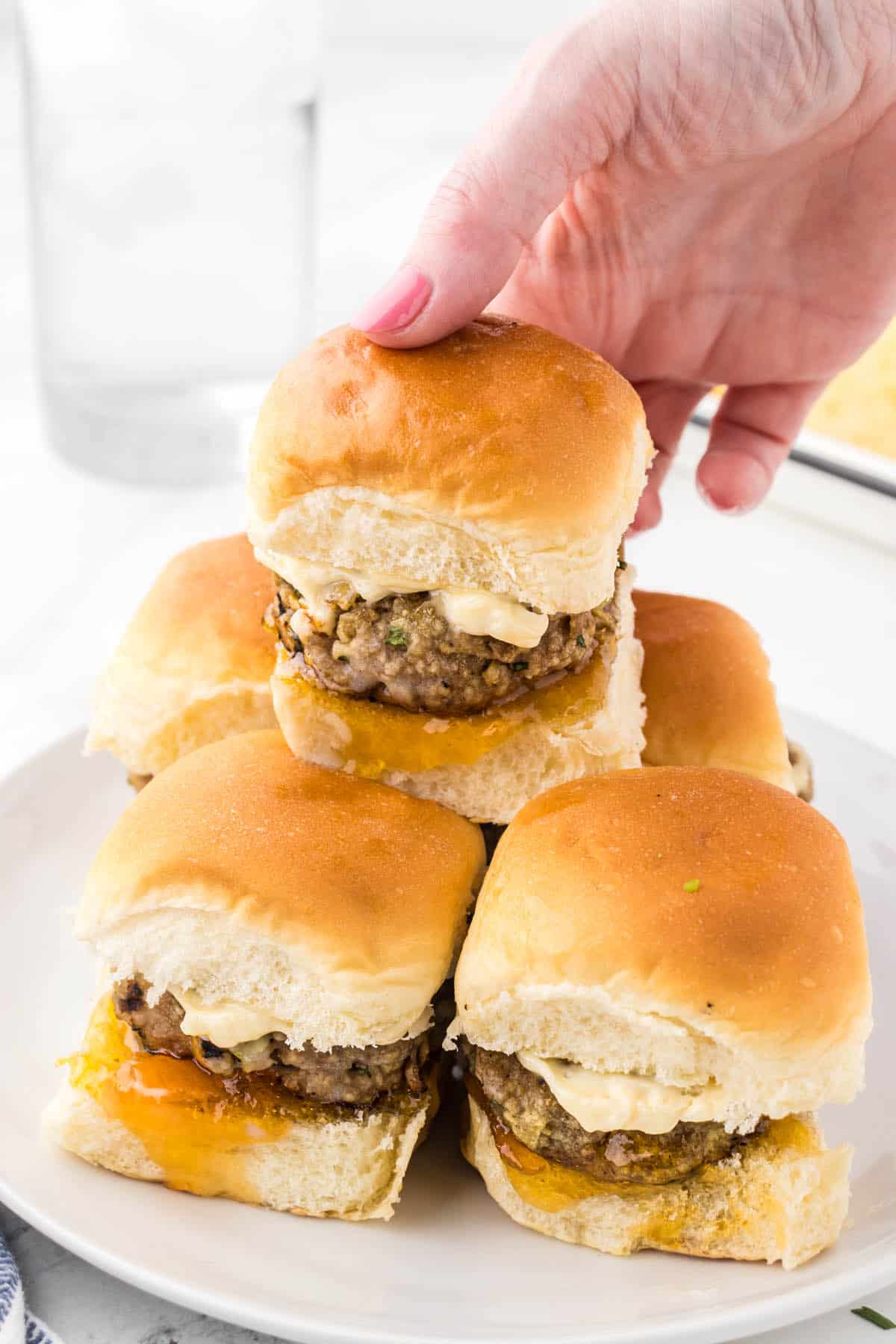 Several ground turkey sliders on Hawaiian rolls on a plate. They are slathered with marmalade and mayonnaise. A hand is reaching in to grab a slider.