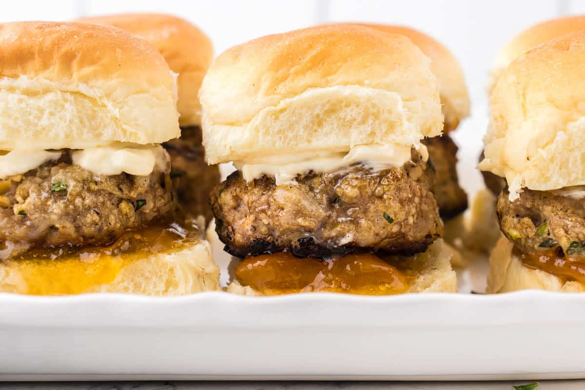 A platter of ground turkey sliders, topped with marmalade and mayonnaise.